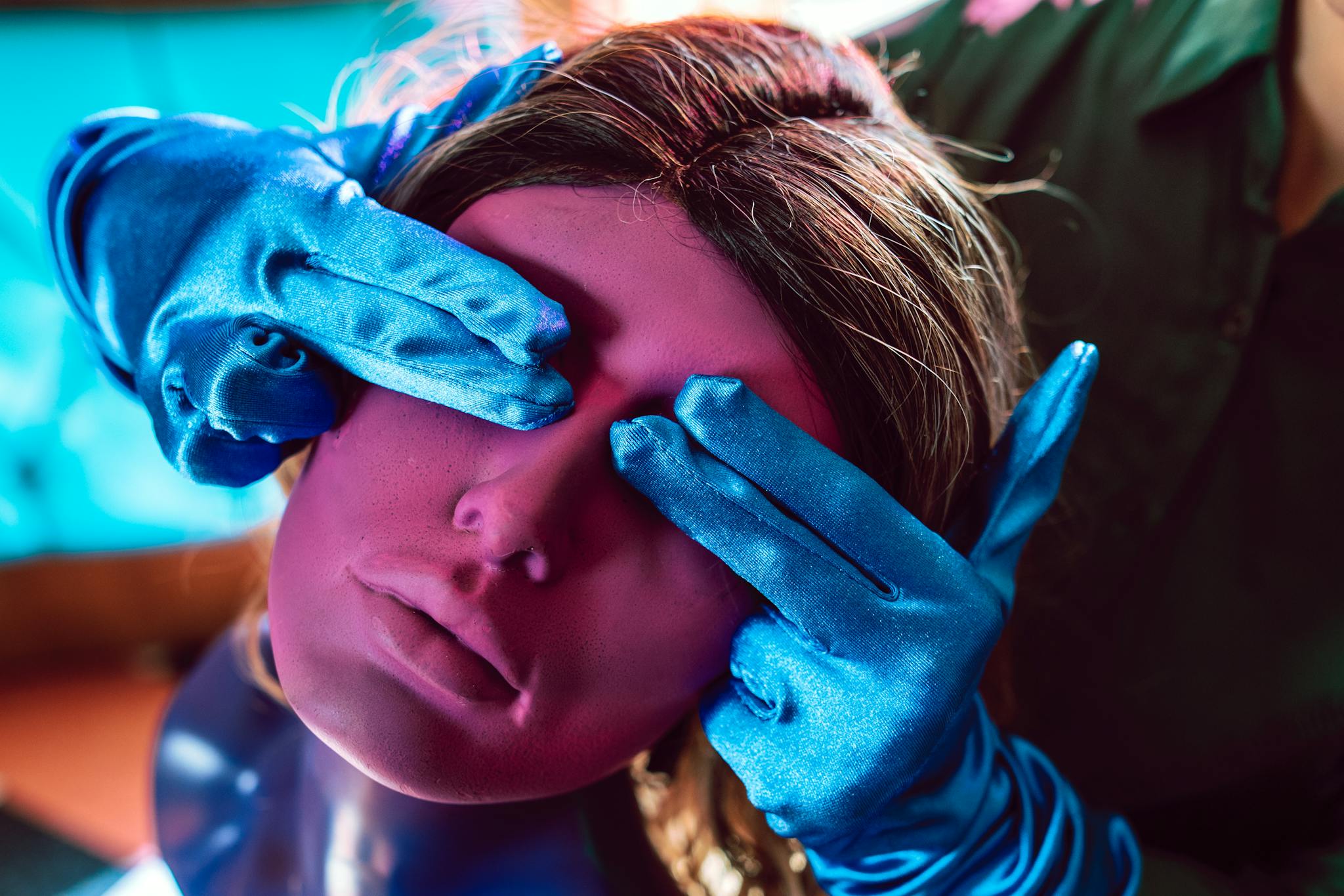 Colorful artistic shot of a wig mannequin being styled with blue gloves.